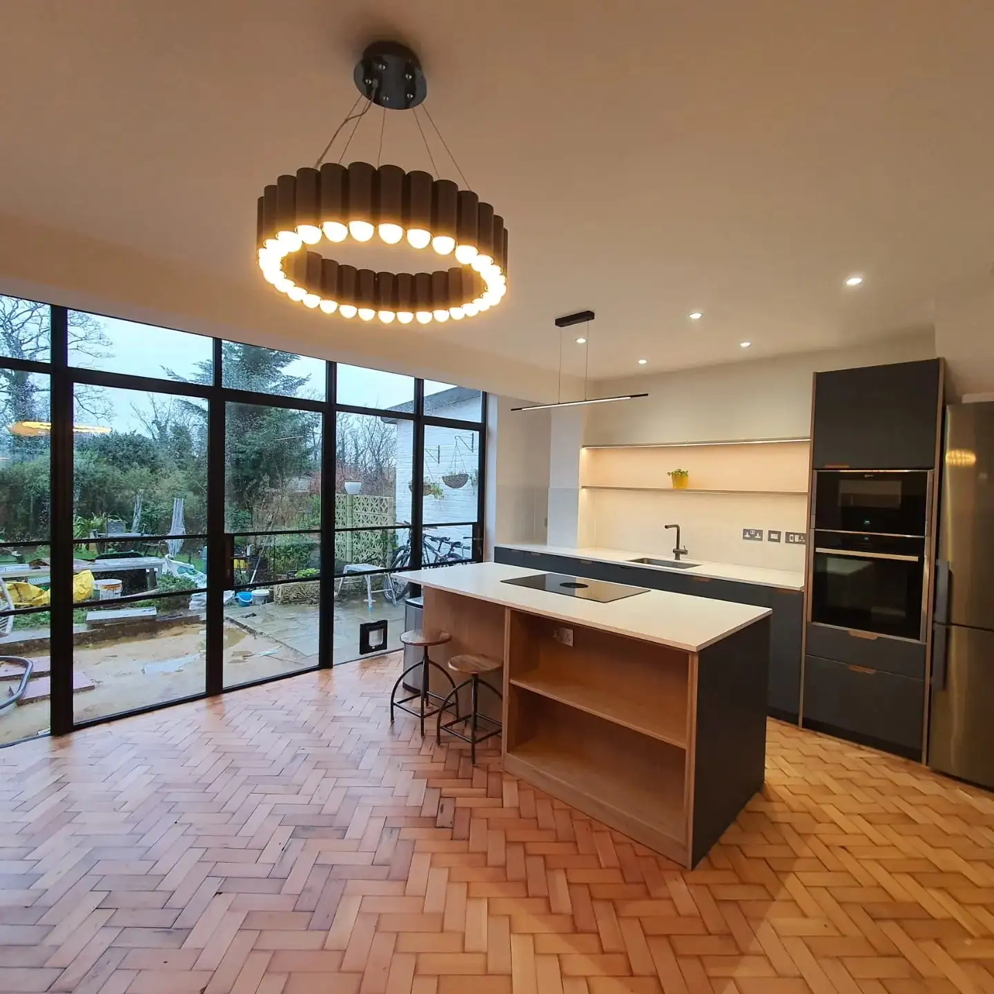 Rear kitchen extension by Two Brothers Construction, with black-framed glazing, an island and herringbone floor