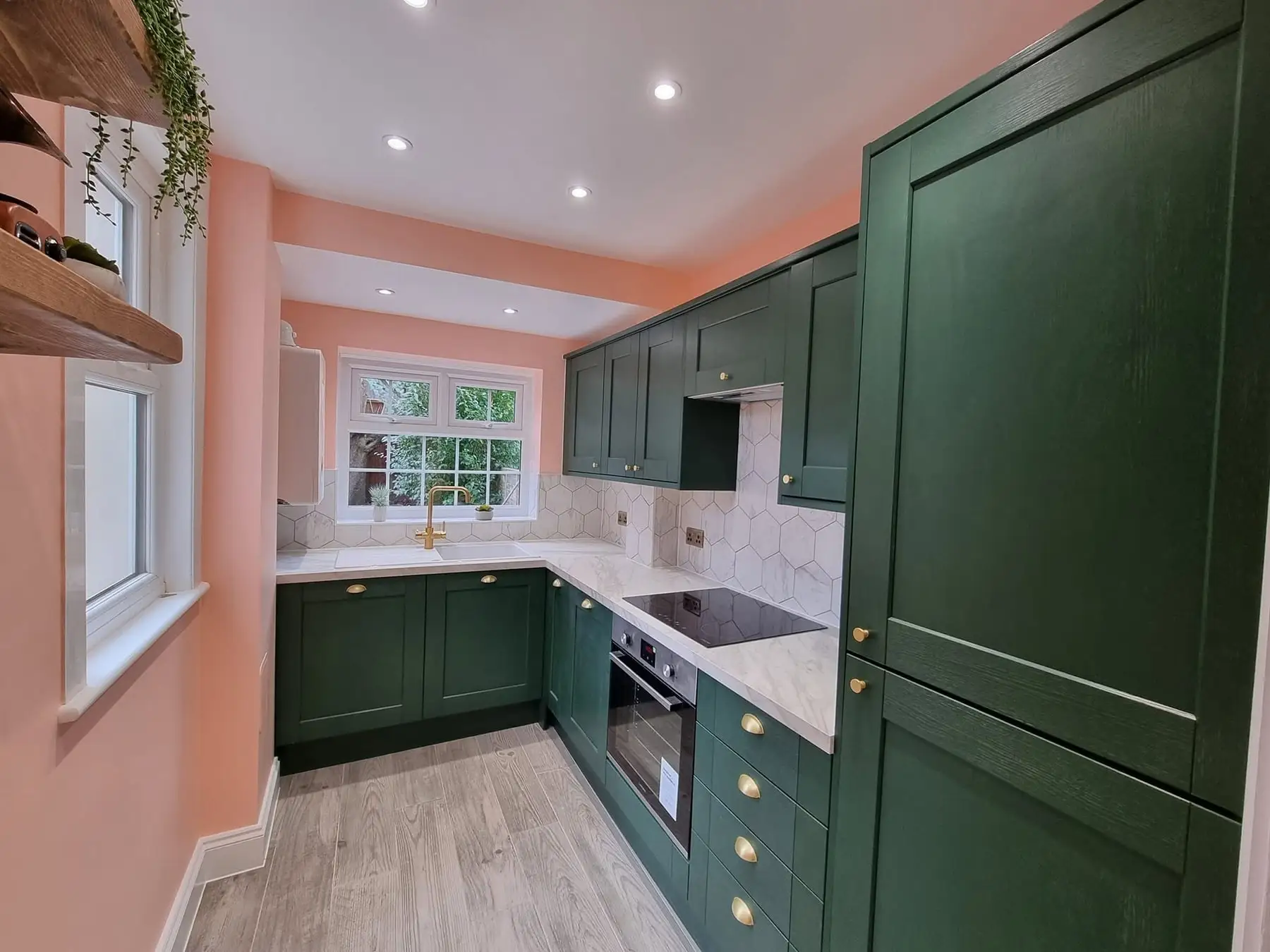 Green shaker kitchen with brass handles and pink walls, fitted by Two Brothers Construction